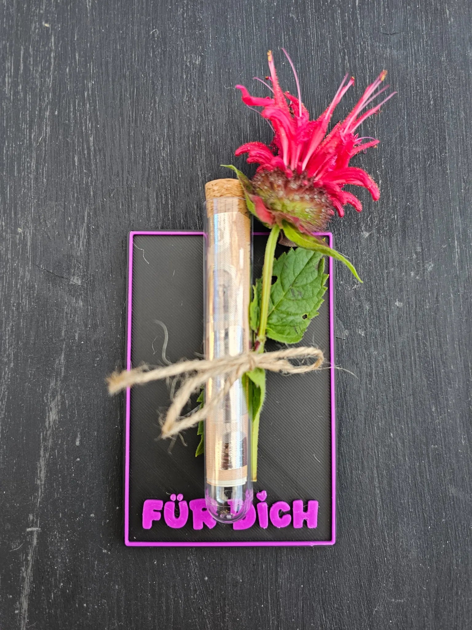 chwarze Karte mit pinker Schrift „FÜR DICH“, Reagenzglas mit Geldschein und Blütendeko
