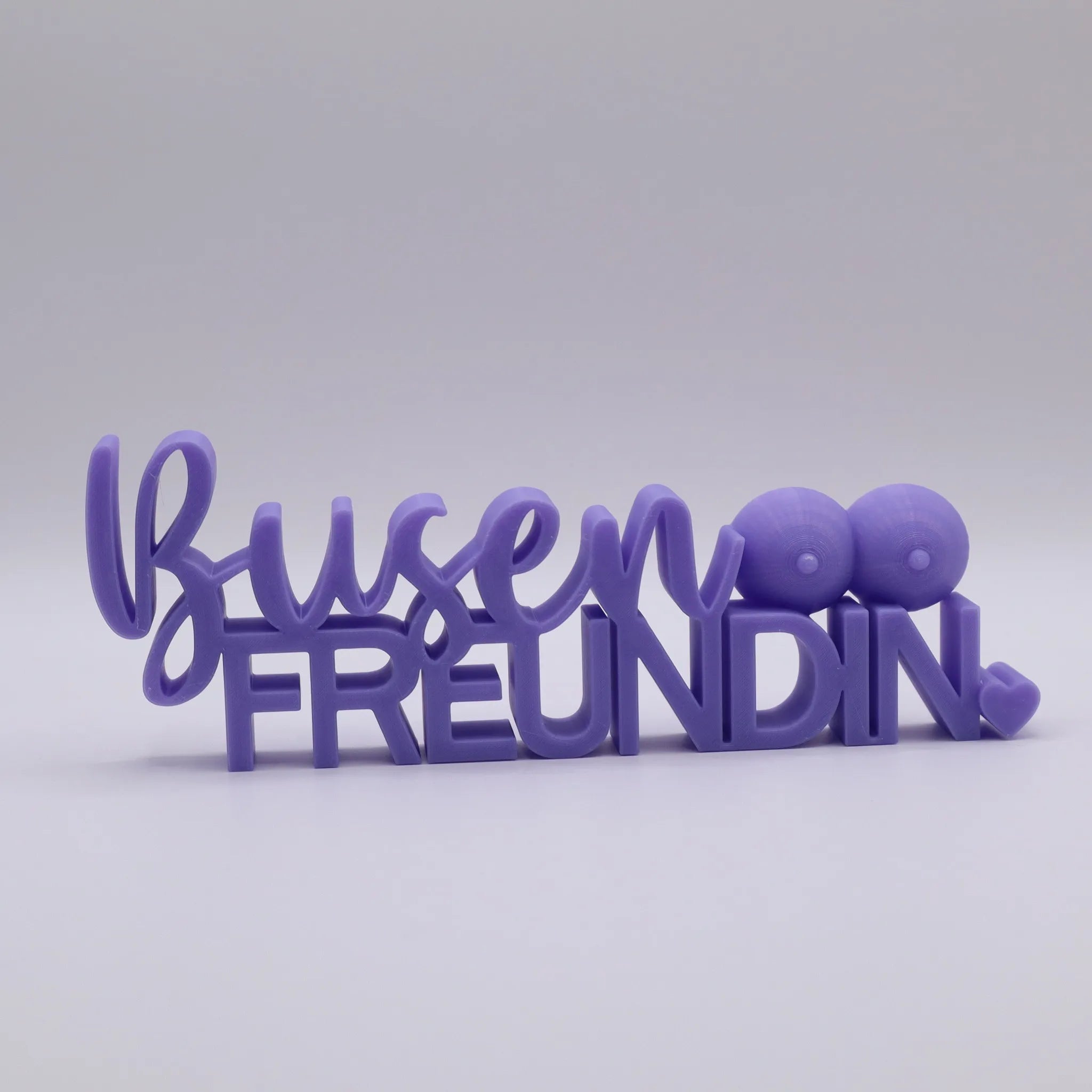 3D-gedrucktes Deko-Statement in Lila mit dem Schriftzug Busenfreundin, verziert mit Busen-Symbolen und Herz