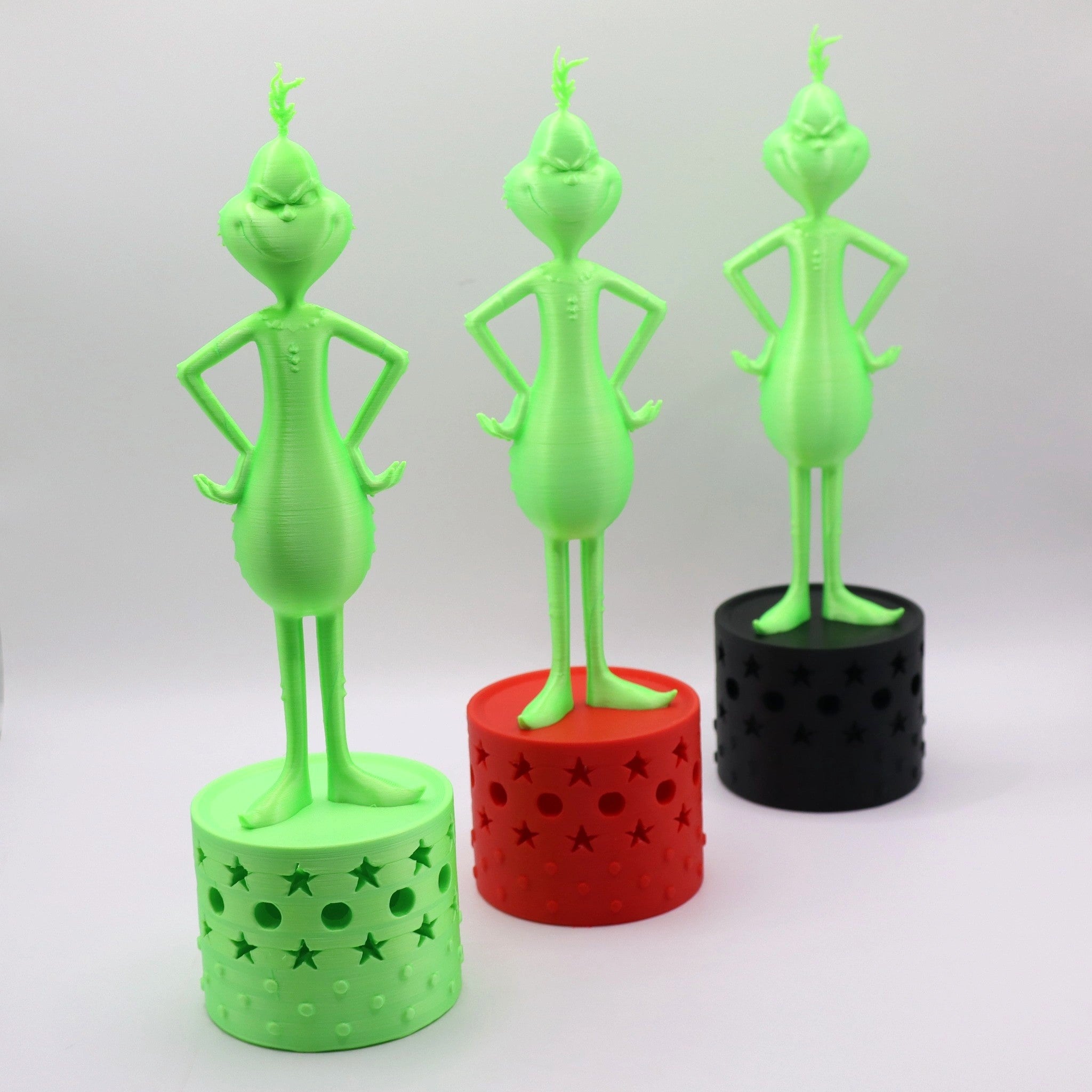 Drei freche Grinch-Figuren in Neon-Grün auf Podesten in Grün, Rot und Schwarz – der ultimative Anti-Weihnachts-Hingucker von Mudivo