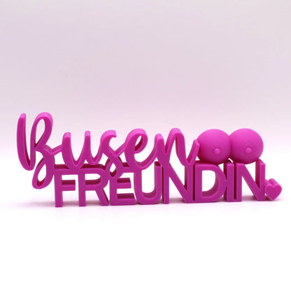 3D-gedrucktes Deko-Statement in Fuchsia mit dem Schriftzug Busenfreundin, verziert mit Busen-Symbolen und Herz