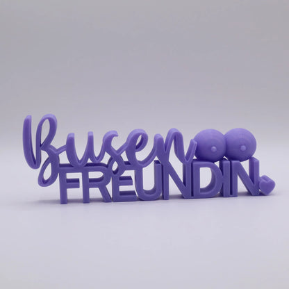 3D-gedrucktes Deko-Statement in Lila mit dem Schriftzug Busenfreundin, verziert mit Busen-Symbolen und Herz
