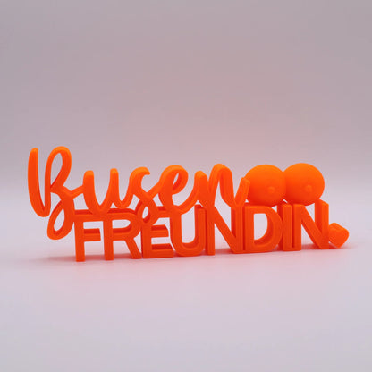 3D-gedrucktes Deko-Statement in Neon Orange mit dem Schriftzug Busenfreundin, verziert mit Busen-Symbolen und Herz