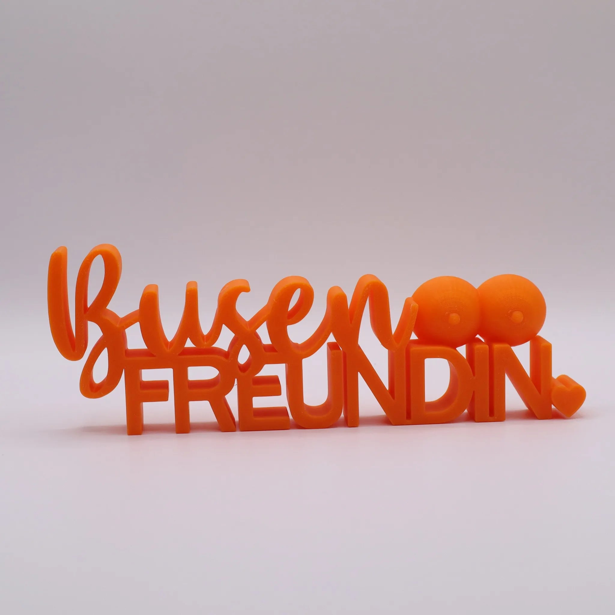 3D-gedrucktes Deko-Statement in Orange mit dem Schriftzug Busenfreundin, verziert mit Busen-Symbolen und Herz