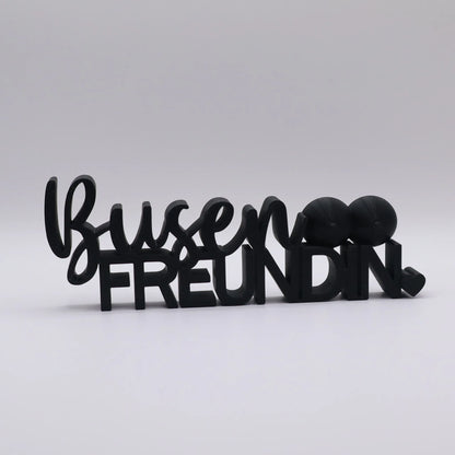 3D-gedrucktes Deko-Statement in Schwarz mit dem Schriftzug Busenfreundin, verziert mit Busen-Symbolen und Herz