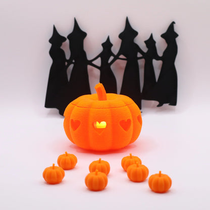 Leuchtender Heart o’-Lantern Kürbis in Orange, dekoriert mit kleinen Mini-Kürbissen und Hexen-Silhouette im Hintergrund